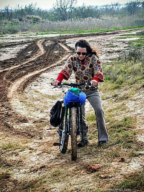 Picture of woman pushing loaded touring bike through muddy road.  