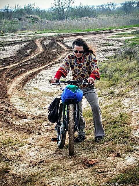 Picture of woman pushing loaded touring bike through muddy road.  